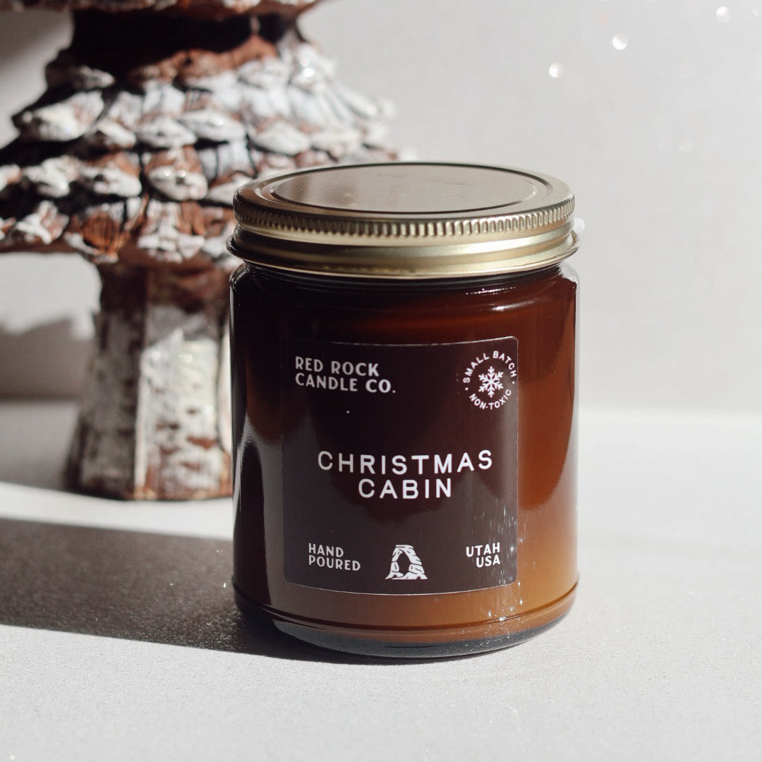 Jar of 'Christmas Cabin' candle from Red Rock Candle Co. with a decorative Christmas tree in the background.