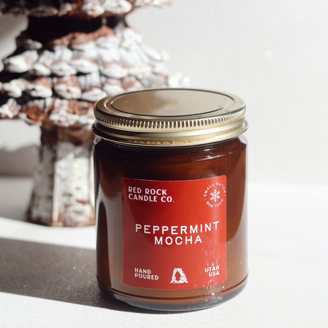 Jar of Red Rock Candle Co Peppermint Mocha candle with a decorative Christmas tree in the background.